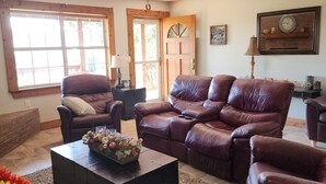 A living room with a brown leather sofa, a black ottoman, and a wooden door. - Great House, Great Vibe. Lake Access/View, Clean, Quiet, Family Pet Friendly. (Sevierville)