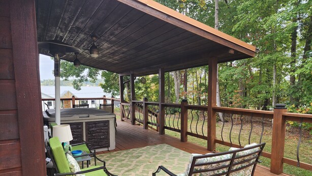 A covered outdoor deck with a wooden railing, a table with chairs, and a view of a building in the background. - Great House, Great Vibe. Lake Access/View, Clean, Quiet, Family Pet Friendly. (Sevierville)