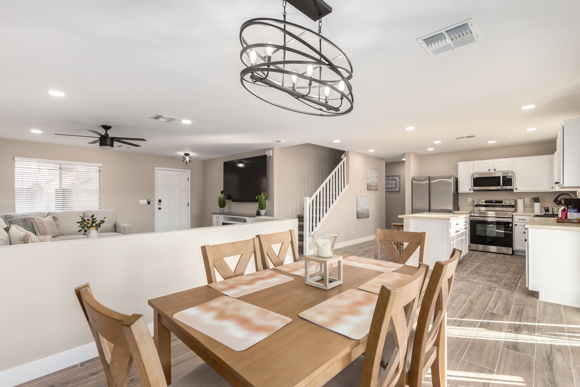 A spacious living area with a dining table, chairs, a chandelier, and a kitchen in the background.