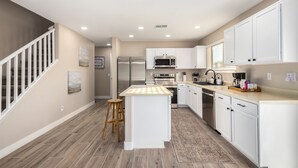 A modern kitchen with white cabinets, stainless steel appliances, and a wooden floor. - Luxury Remodel in Phoenix ~ EV Charger, Putting Green, Family & Pet-Friendly (Phoenix)