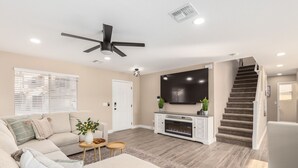 A living room with a sofa, a coffee table, a fireplace, a TV, and a staircase. - Luxury Remodel in Phoenix ~ EV Charger, Putting Green, Family & Pet-Friendly (Phoenix)