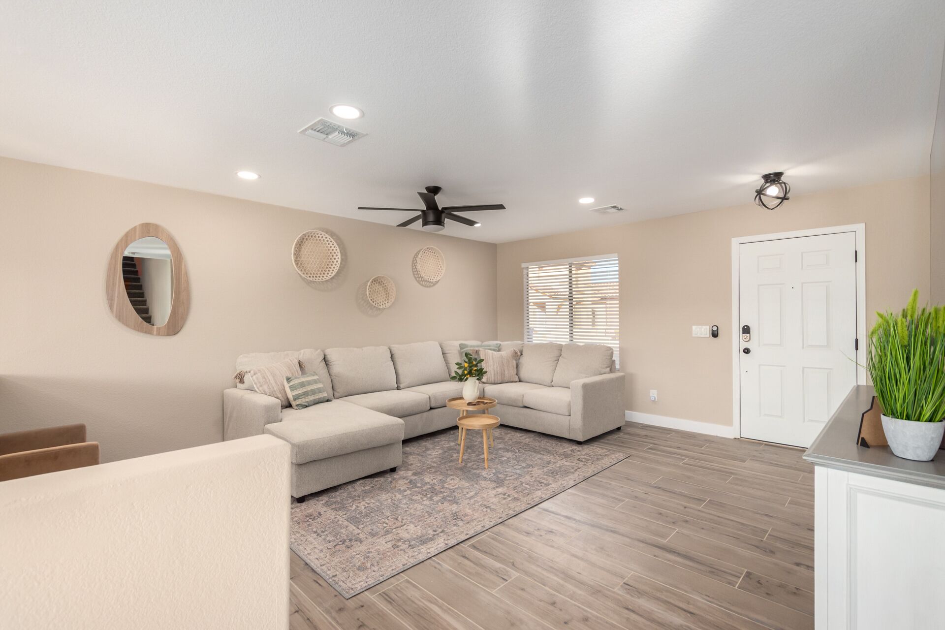 A modern living room with a sectional sofa, a ceiling fan, recessed lighting, and a wooden floor.