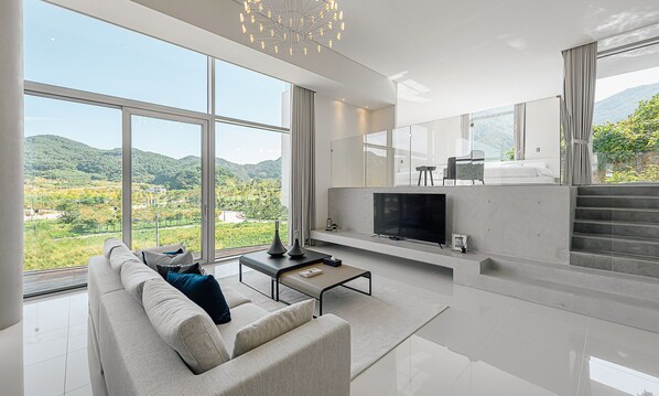 Una sala de estar moderna con un televisor grande, asientos cómodos y vistas a un paisaje verde a través de amplias ventanas.
