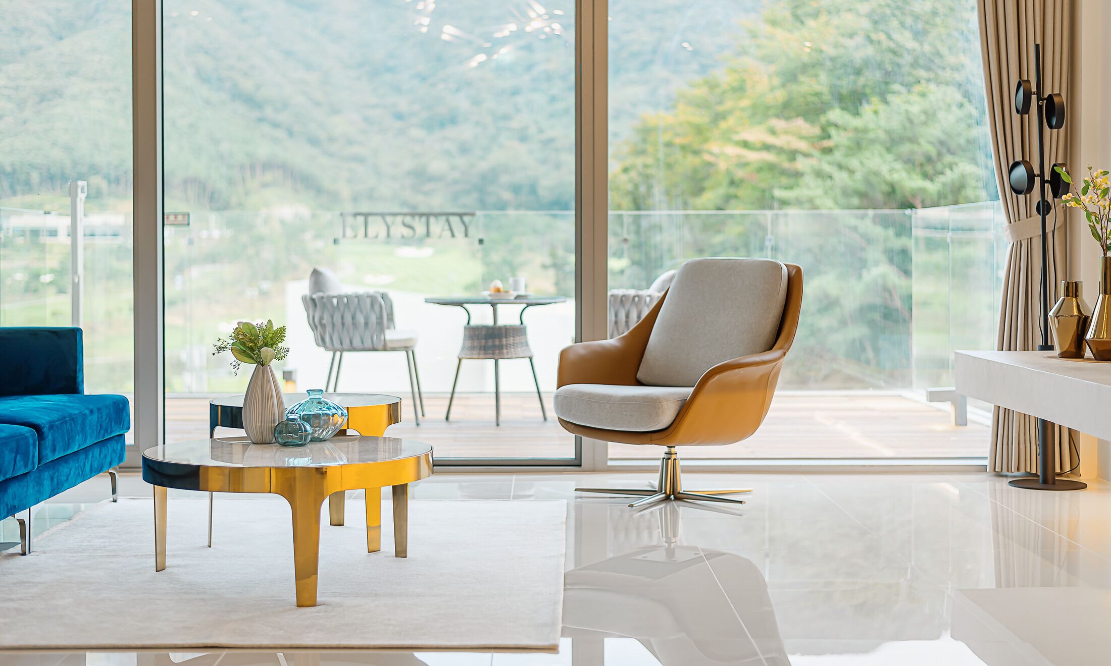 A modern living room with a large window, a blue sofa, a round coffee table, and a white armchair.