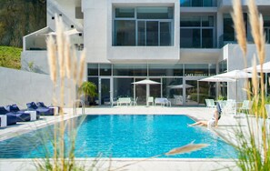Un hotel moderno con piscina, sillones de descanso y sombrillas.