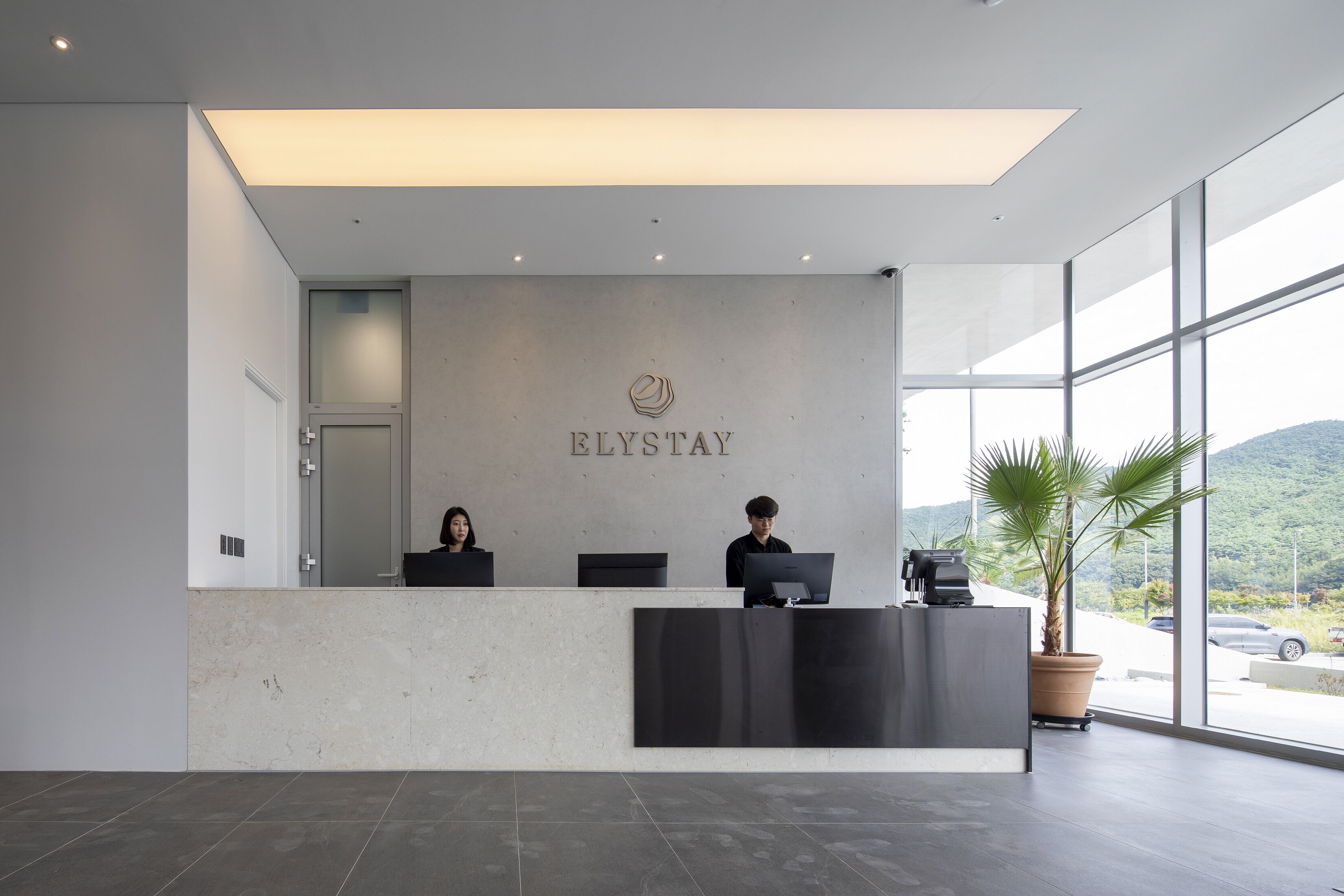 A reception desk with a modern design, a logo above it, and a view of the outdoors through large windows.