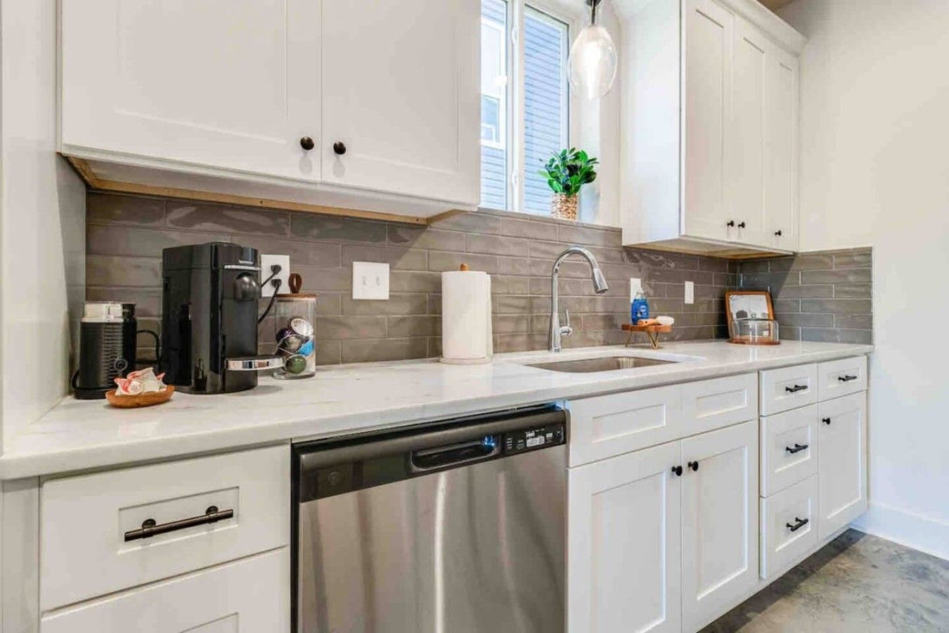 A modern kitchen with white cabinetry, a stainless steel dishwasher, and a gray-tiled backsplash.