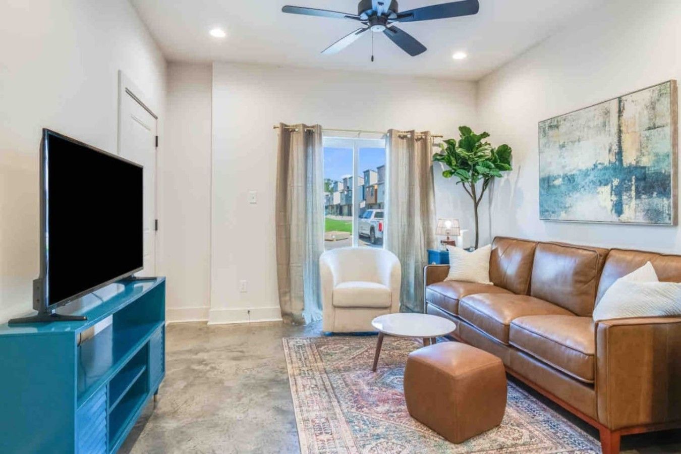 A living room with a flat-screen TV, a leather sofa, a coffee table, and a patterned rug.