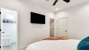 Une chambre à coucher avec un lit, un téléviseur fixé au mur et un ventilateur de plafond.