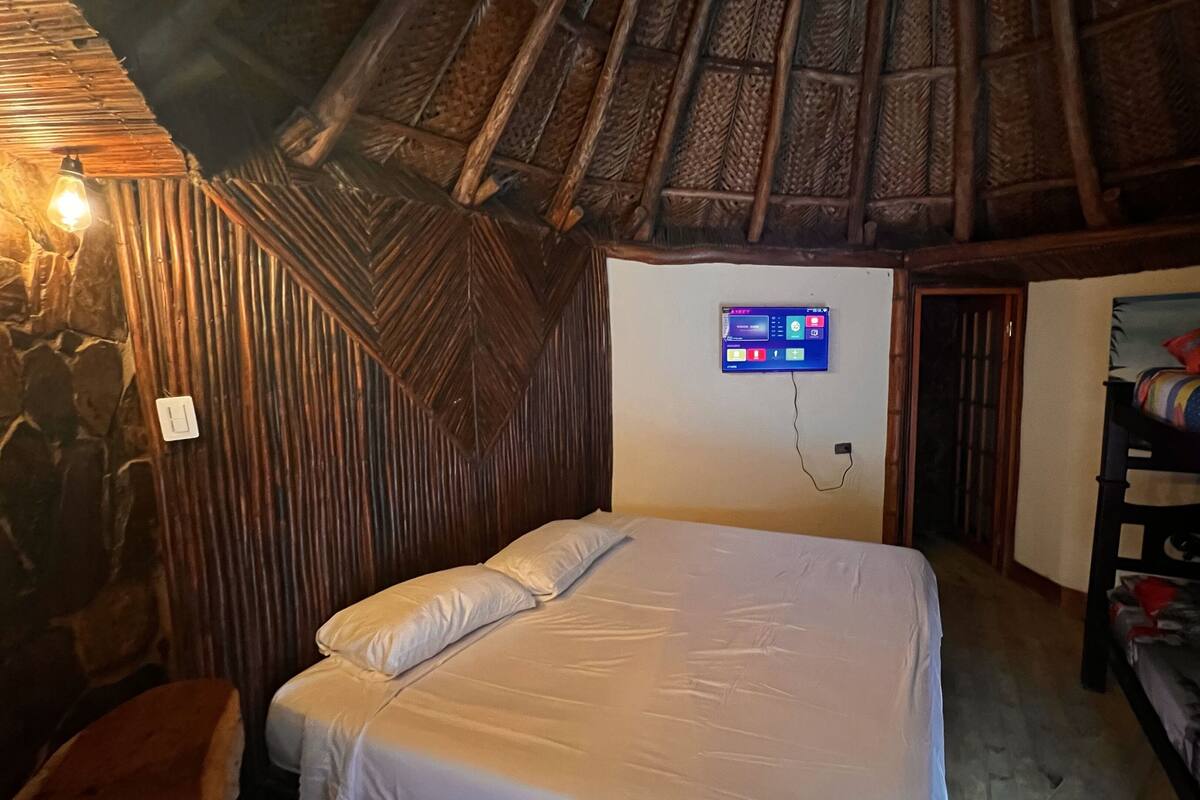 A room with a bed, a bunk bed, a wall-mounted TV, and a rustic wooden ceiling.