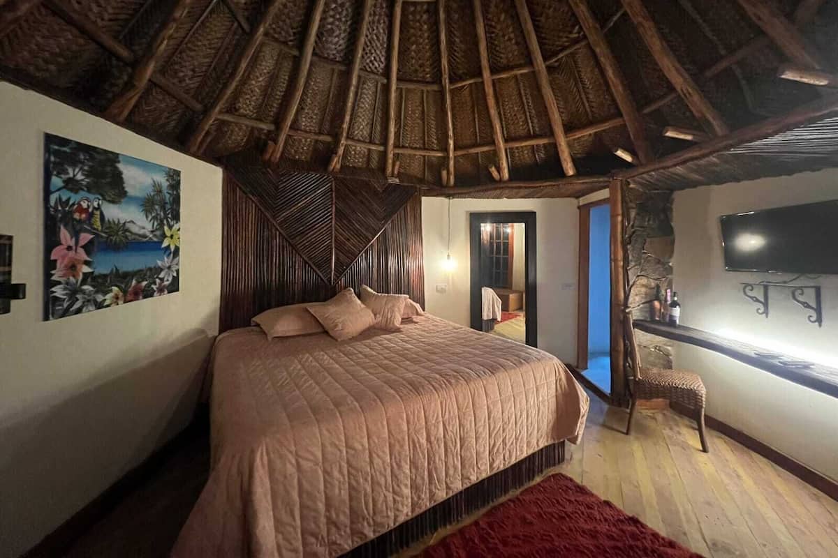 A bedroom with a bed, a painting, a TV, and a stone wall.