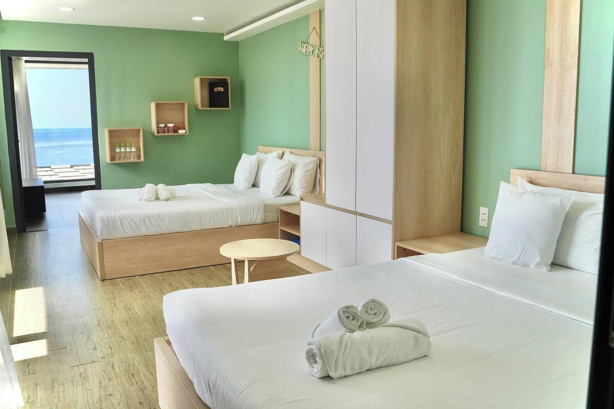 A hotel room with two beds, a small round table, wooden headboards, and a view of the sea.