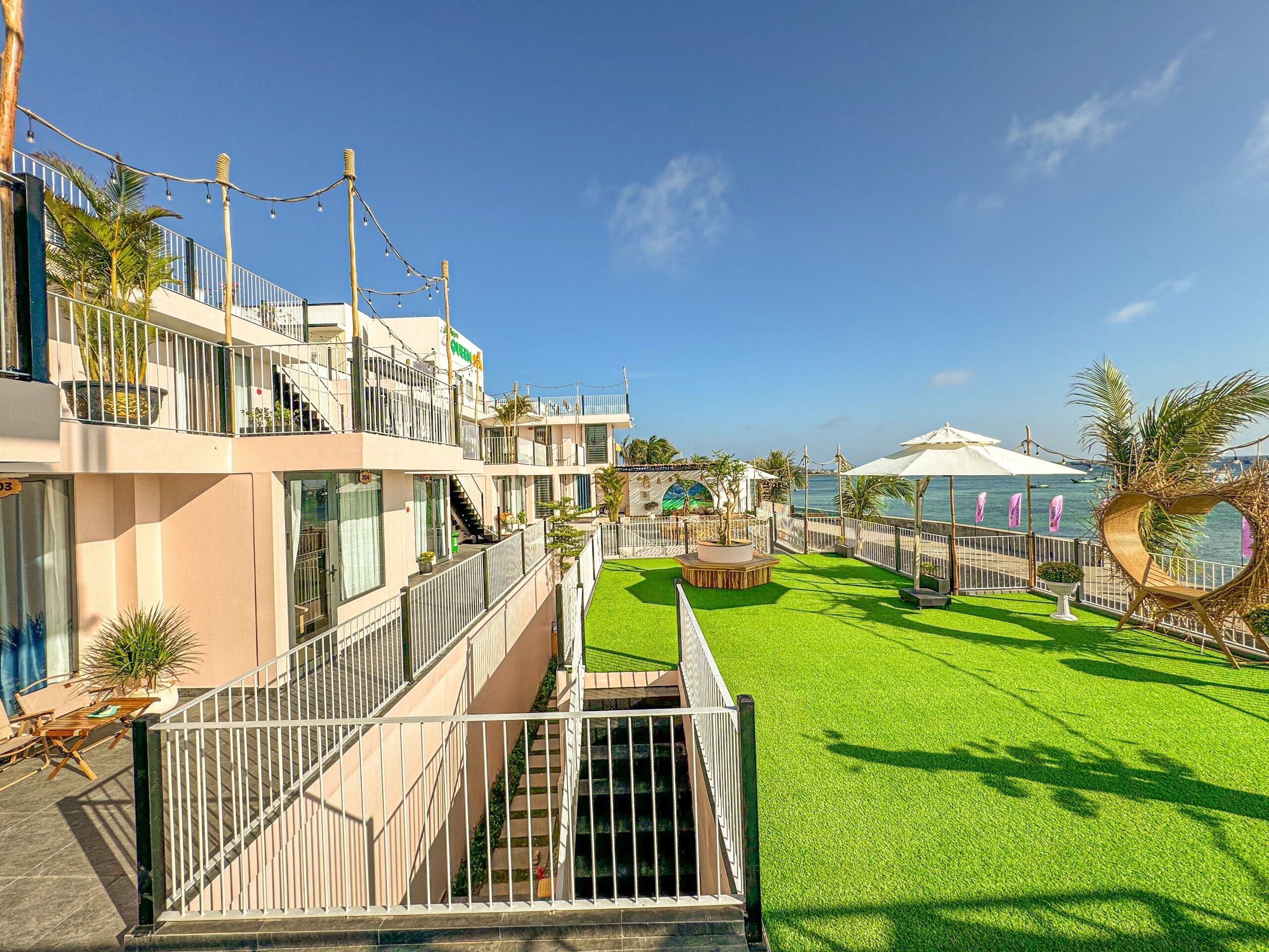 Un hotel con varios balcones, un patio central con césped artificial y vistas al mar.