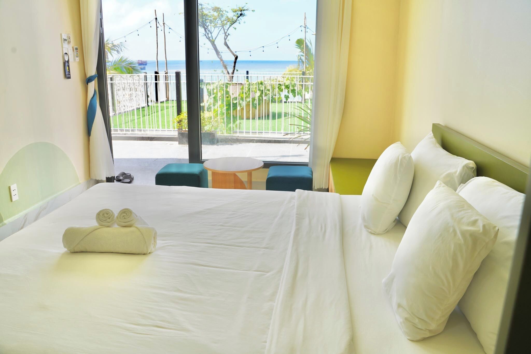 A hotel room with a bed, pillows, a small round table, and a view of the ocean through large windows.
