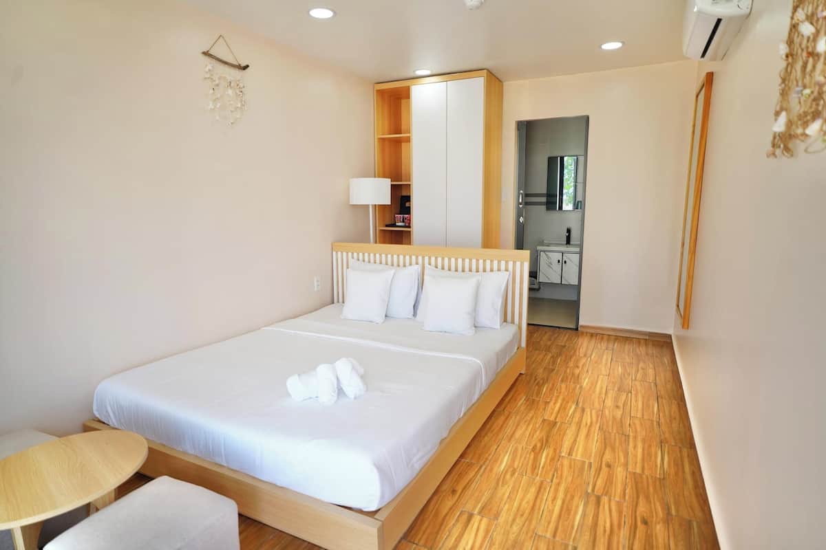 A hotel room with a wooden bed, a bedside table, a small round table, and a mirror.
