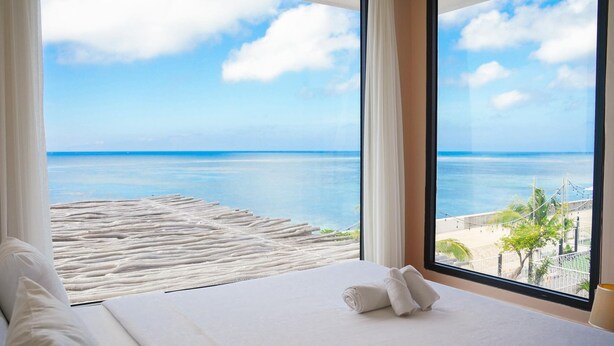 A hotel room with a large window offering a view of the ocean and a sandy beach. - Resort Queen Sea (Phu Quy)