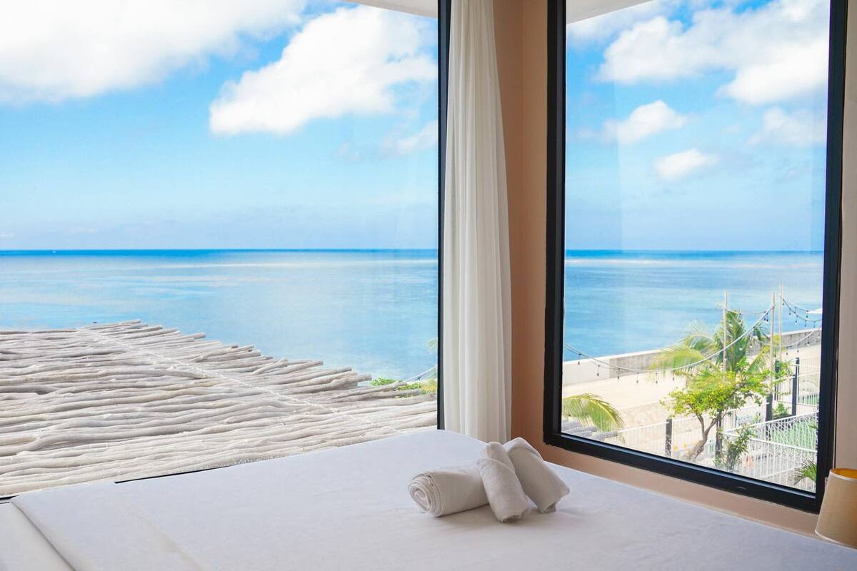 A hotel room with a large window offering a view of the ocean and a sandy beach.