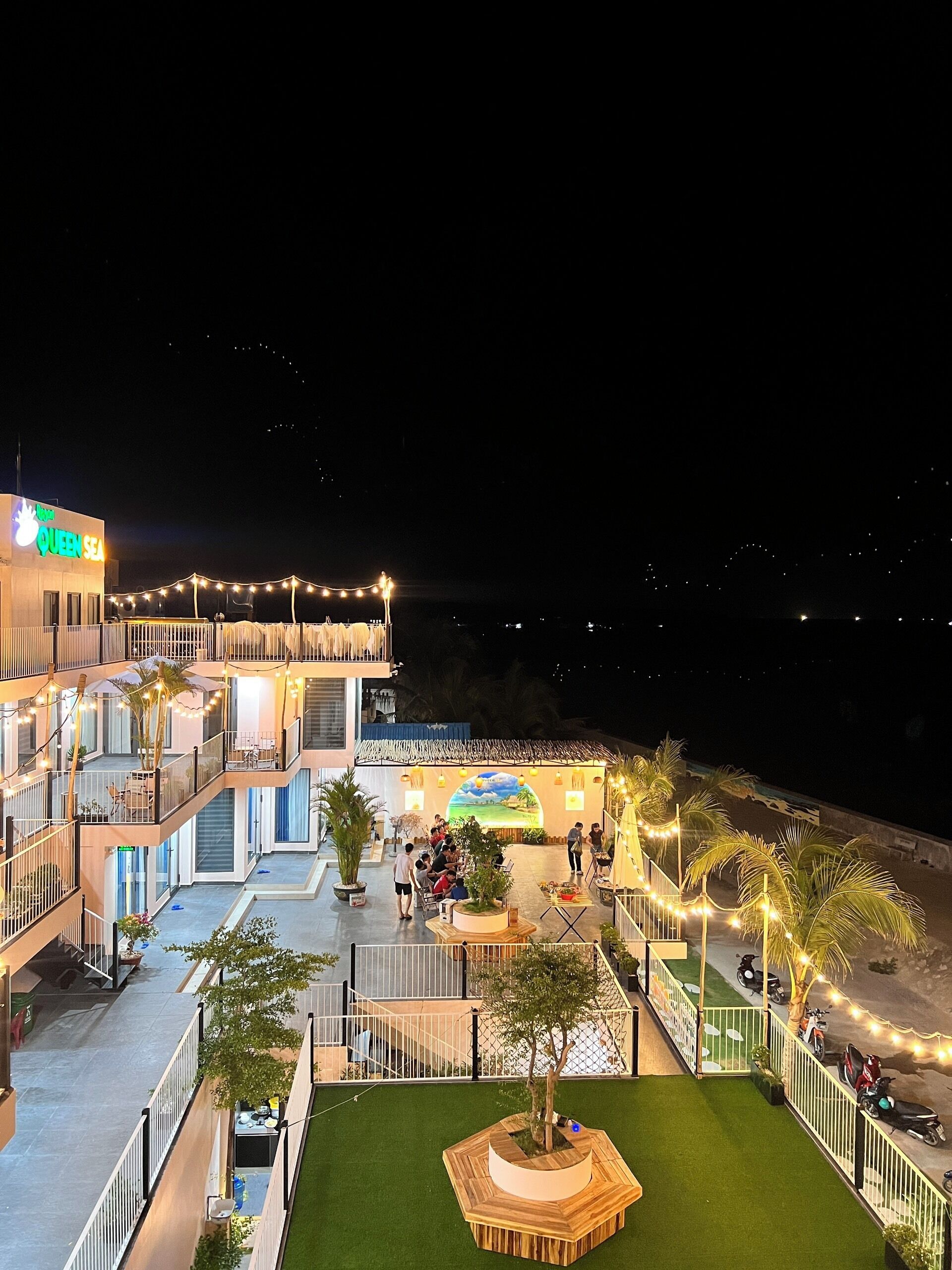 A multi-level hotel with outdoor seating areas, palm trees, and string lights.