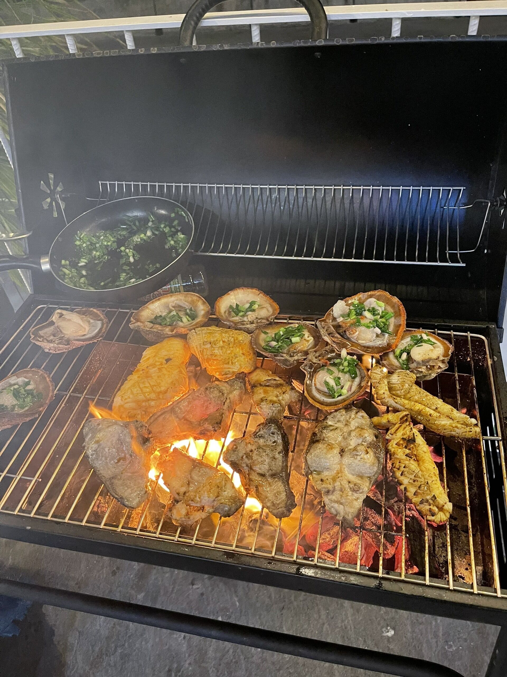 A grill with various meats and seafood being cooked over an open flame.