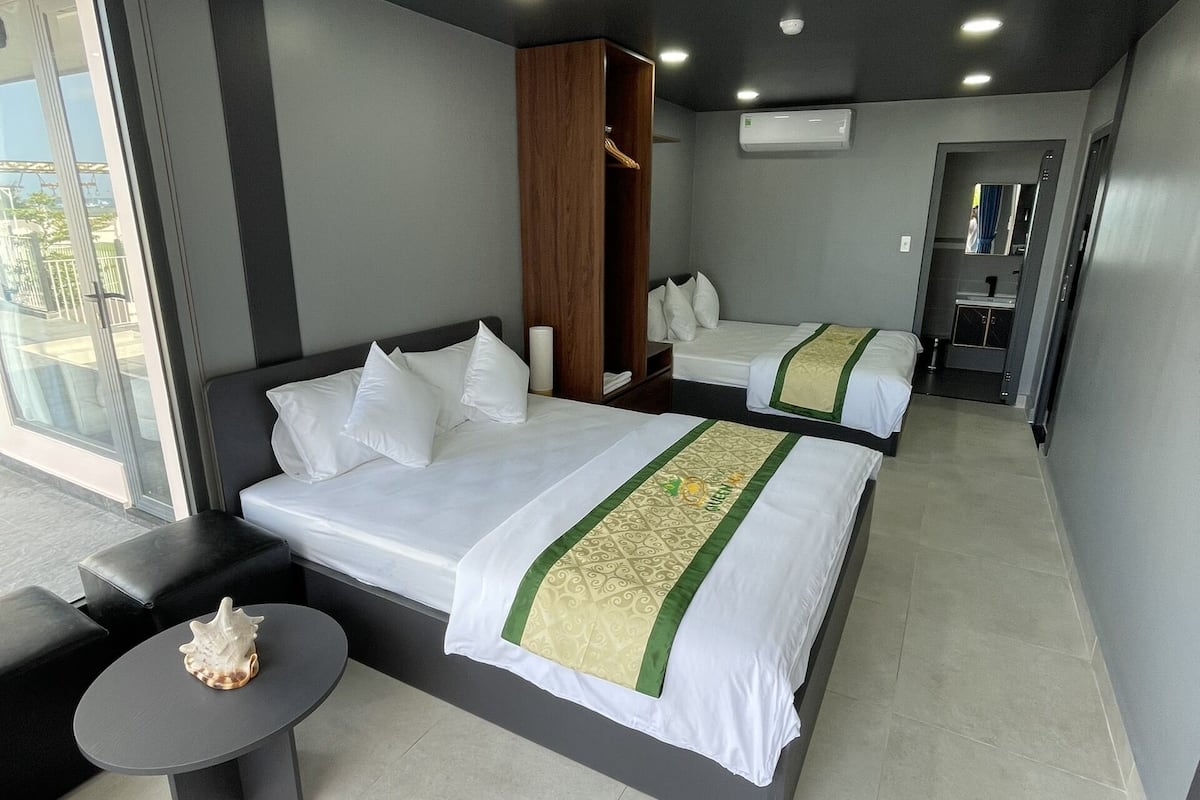 A modern hotel room with two beds, a seating area, and a view of the outdoors.