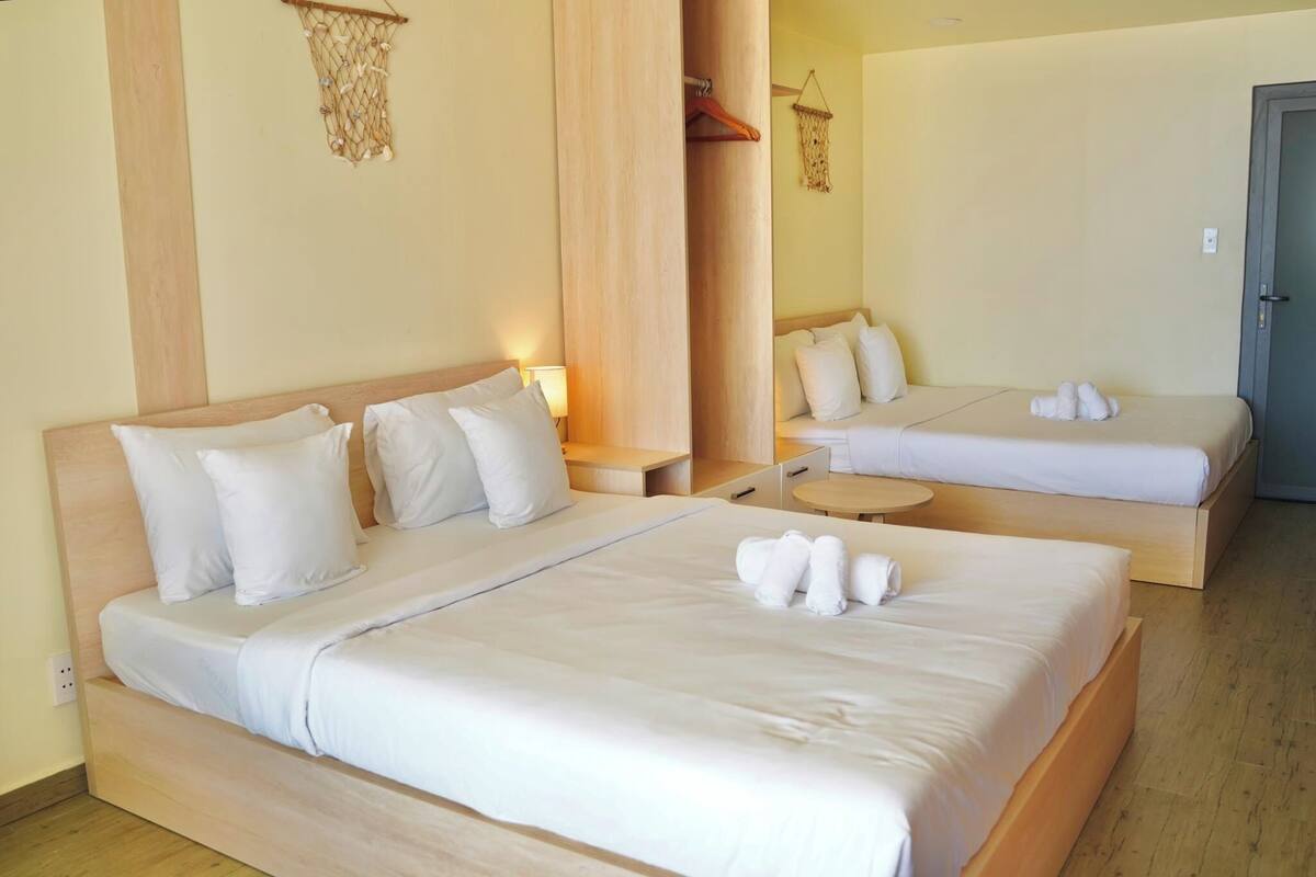 A hotel room with two beds, each with white bedding and pillows. There are bedside tables with lamps, a small round table, and a wardrobe with a mirror.