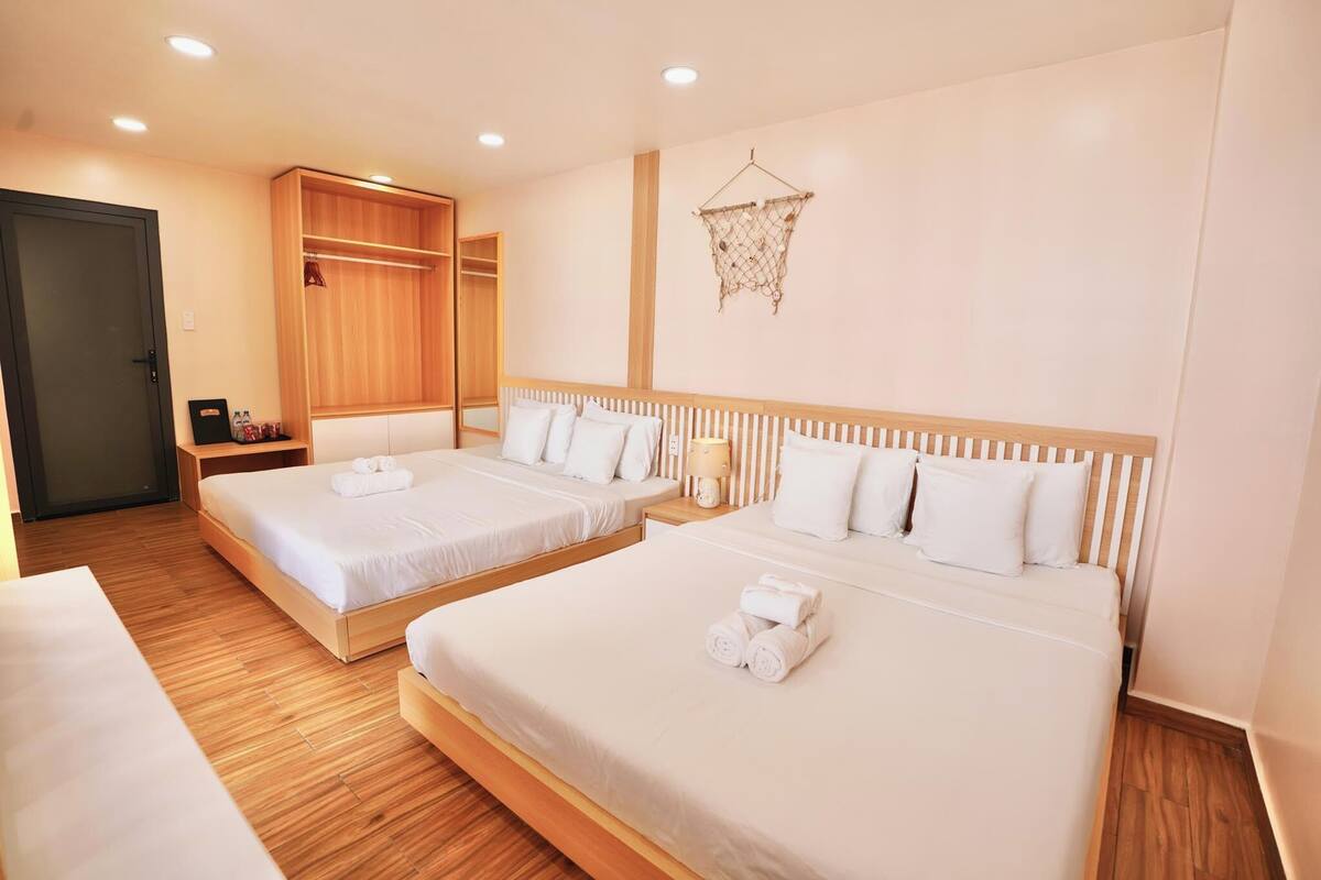 A hotel room with two beds, wooden flooring, a wardrobe, and a hanging decorative item.