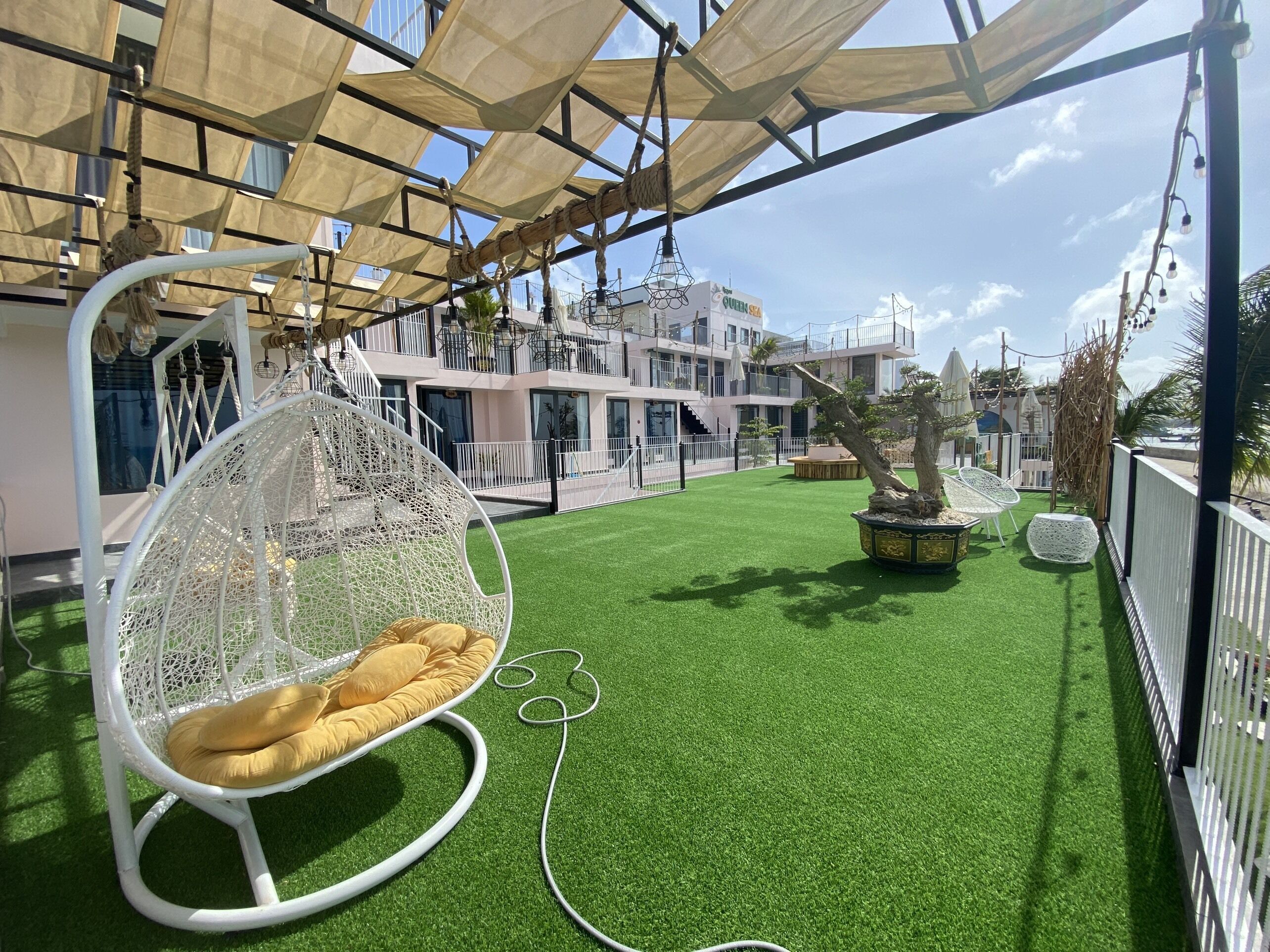 Een terras op het dak met kunstgras, een hangstoel en een plant in een pot.
