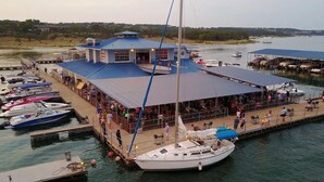 A marina with docked boats, a covered dining area, and a sailboat. - Billie Jean, Lake Travis - Sleeps 8 Lake Access (Point Venture)