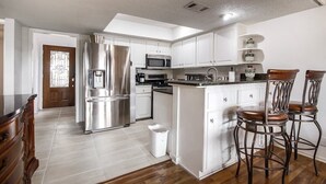 A modern kitchen with white cabinets, stainless steel appliances, and a bar area with stools. - Billie Jean, Lake Travis - Sleeps 8 Lake Access (Point Venture)