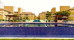 A swimming pool surrounded by yellow buildings with a clear sky. - The Sun Resort - Super Apartamento de 2 Quartos (Brasília)