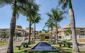 A hotel with a swimming pool surrounded by palm trees and a clear blue sky. - The Sun Resort - Super Apartamento de 2 Quartos (Brasília)