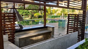 Zona junto a la piscina con jacuzzi integrado, pérgola de madera y mobiliario exterior.