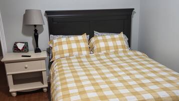 Un lit bien fait, recouvert d’une couvre-lit à carreaux, une table de chevet avec une lampe et une petite table de chevet sur laquelle se trouve une boîte de mouchoirs.