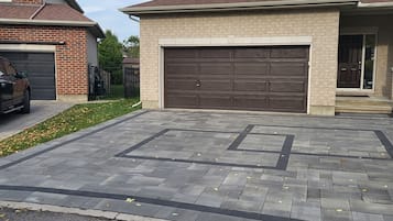 Une allée menant à une maison et à un garage, avec une maison en briques sur la gauche et une maison de couleur beige sur la droite.
