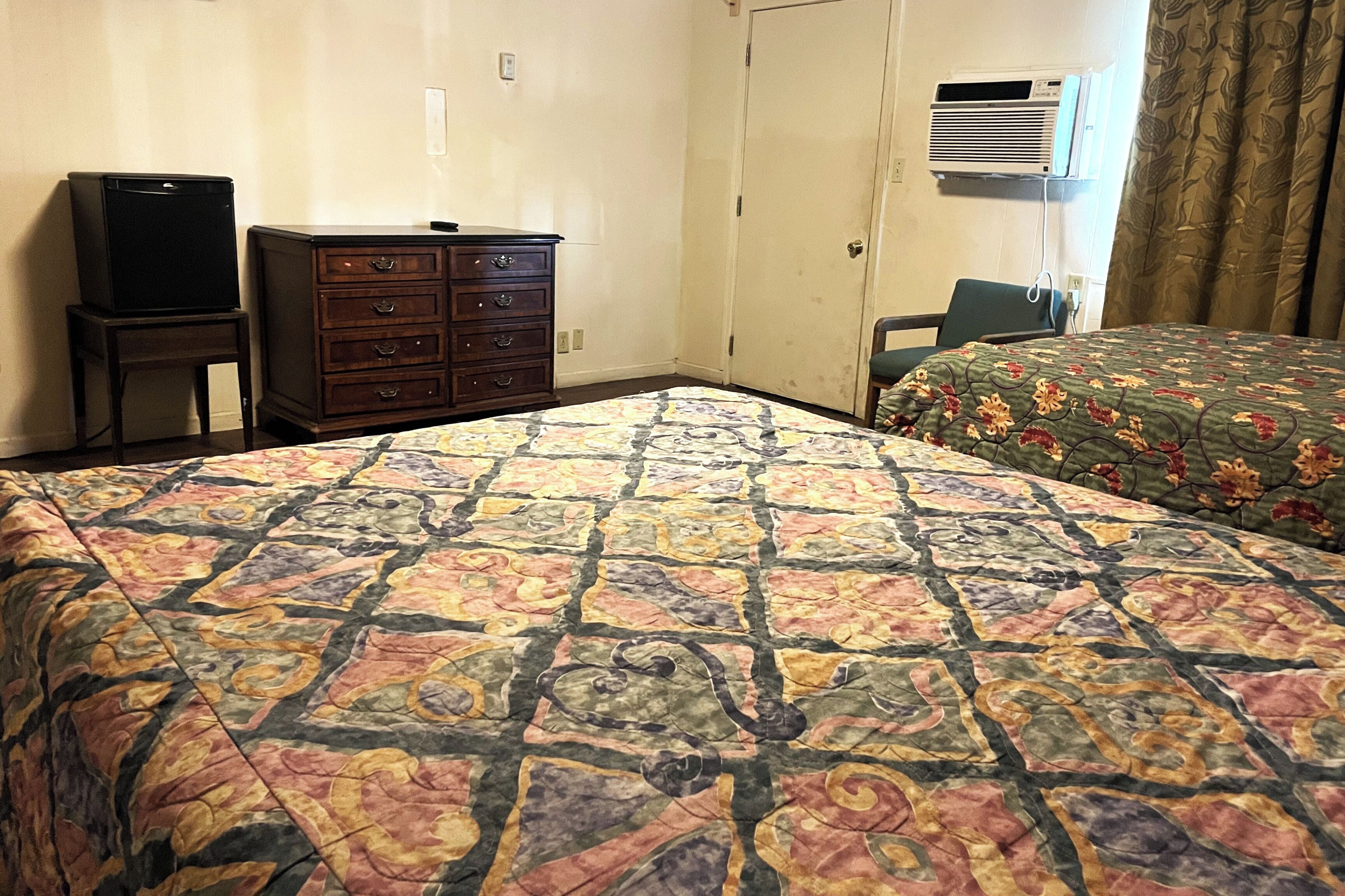 A hotel room with a bed, a dresser, a television, and an air conditioning unit.