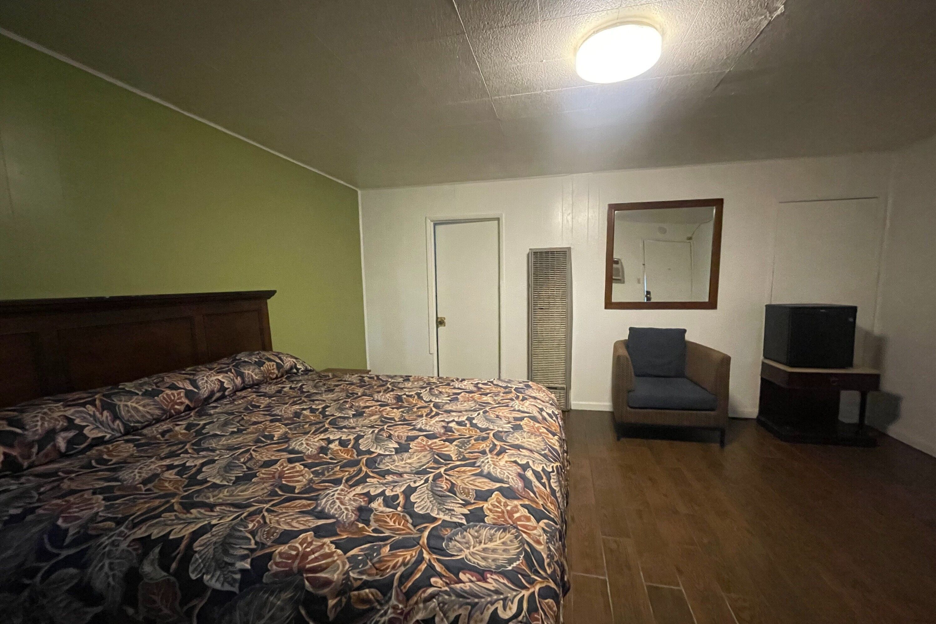 A bedroom with a bed, a chair, a television, and a door.