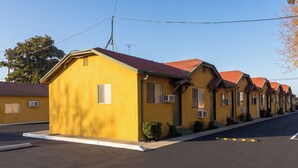 Una hilera de edificios amarillos de un piso y techos rojos, probablemente un motel o hotel pequeño, bajo un cielo despejado y sin personas ni decoraciones visibles.