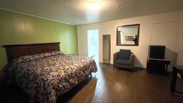 Un dormitorio con una cama, una silla, un televisor y un espejo.