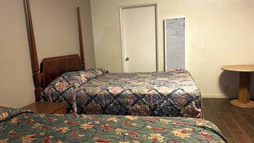 A room with two beds, a wooden chair, a small round table, and a door.