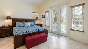 A bedroom with a large bed, a ceiling fan, a red bench, and a view of the outside through the sliding glass door. - Beach Breezes: Pool & Spa, Ping Pong, 3 Blocks to Beach! (Holmes Beach)