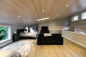 Une chambre moderne avec un plafond en bois, un grand lit, un canapé noir et un téléviseur.