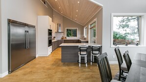 A modern kitchen with a large island, stainless steel appliances, and a dining area with a wooden table and chairs. - Sooke Waterfront Retreat – Hot Tub & Dock Access (Sooke)