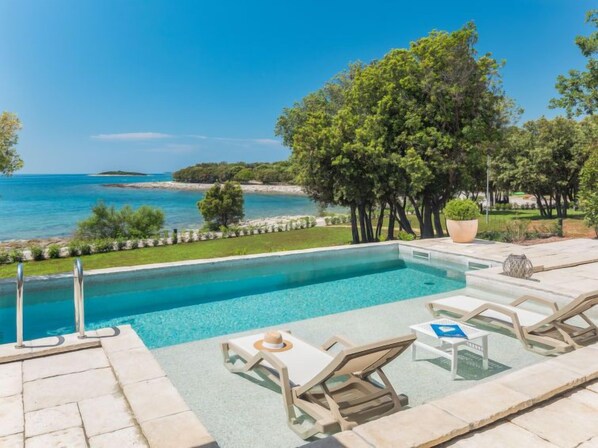 A swimming pool with lounge chairs and a view of the sea.