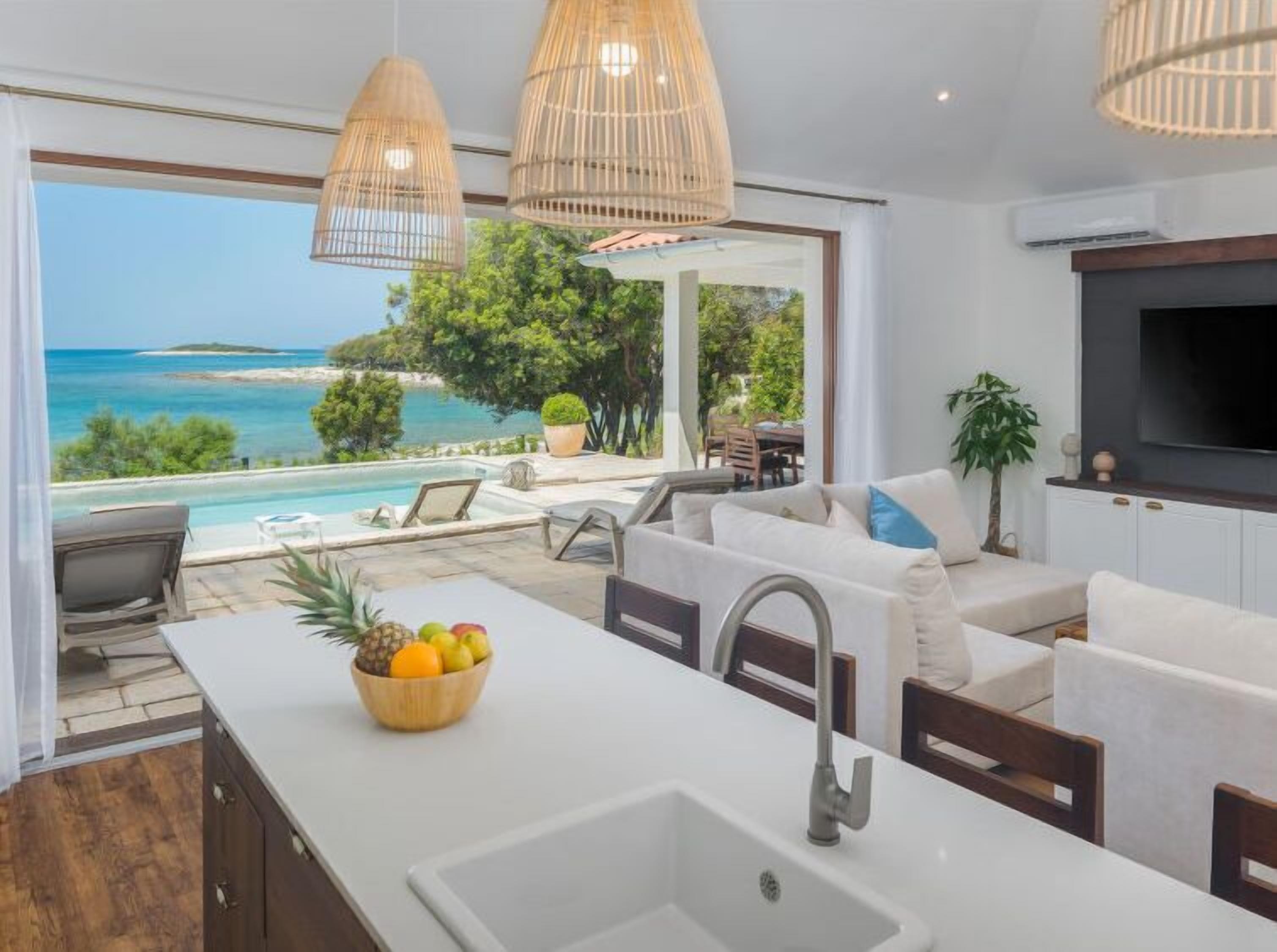 Een moderne keuken met een groot eiland, een inbouwspoelbak en uitzicht op een zwembad en strand.