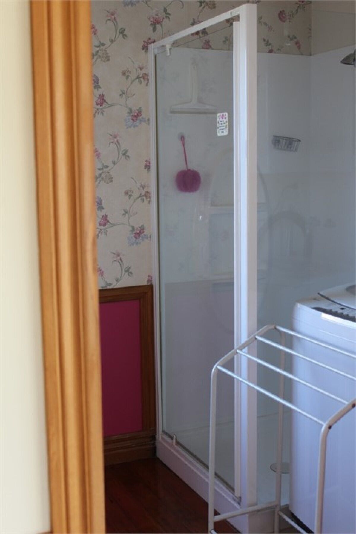 Habitació amb zona de dutxa, estendal blanc i paper pintat floral.