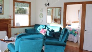 Ein Zimmer mit einem Türkis-farbenen Sofa, einem Holztisch mit Lampe und einem Bett mit floralem Überwurf.