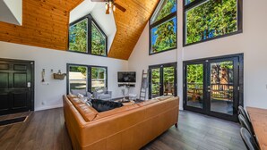 Un salon spacieux avec un grand canapé en cuir marron, un plafond en bois et de grandes fenêtres offrant une vue sur l’extérieur.