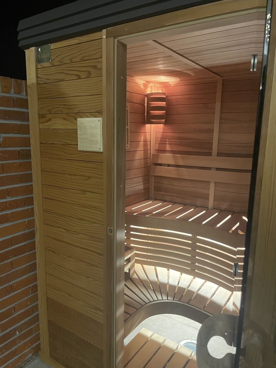 A sauna with a wooden interior, a bench, and a wall-mounted light fixture.
