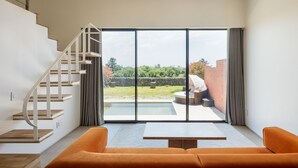 Een moderne woonkamer met een trap, een grote schuifpui naar een terras en uitzicht op een tuin.