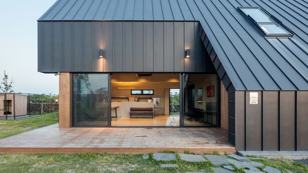 Een modern huis met een ruime glazen voordeur, een zichtbare keuken en een kleine hond die buiten zit.